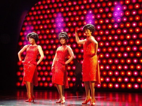 Three performers in red sequinned dresses on stage